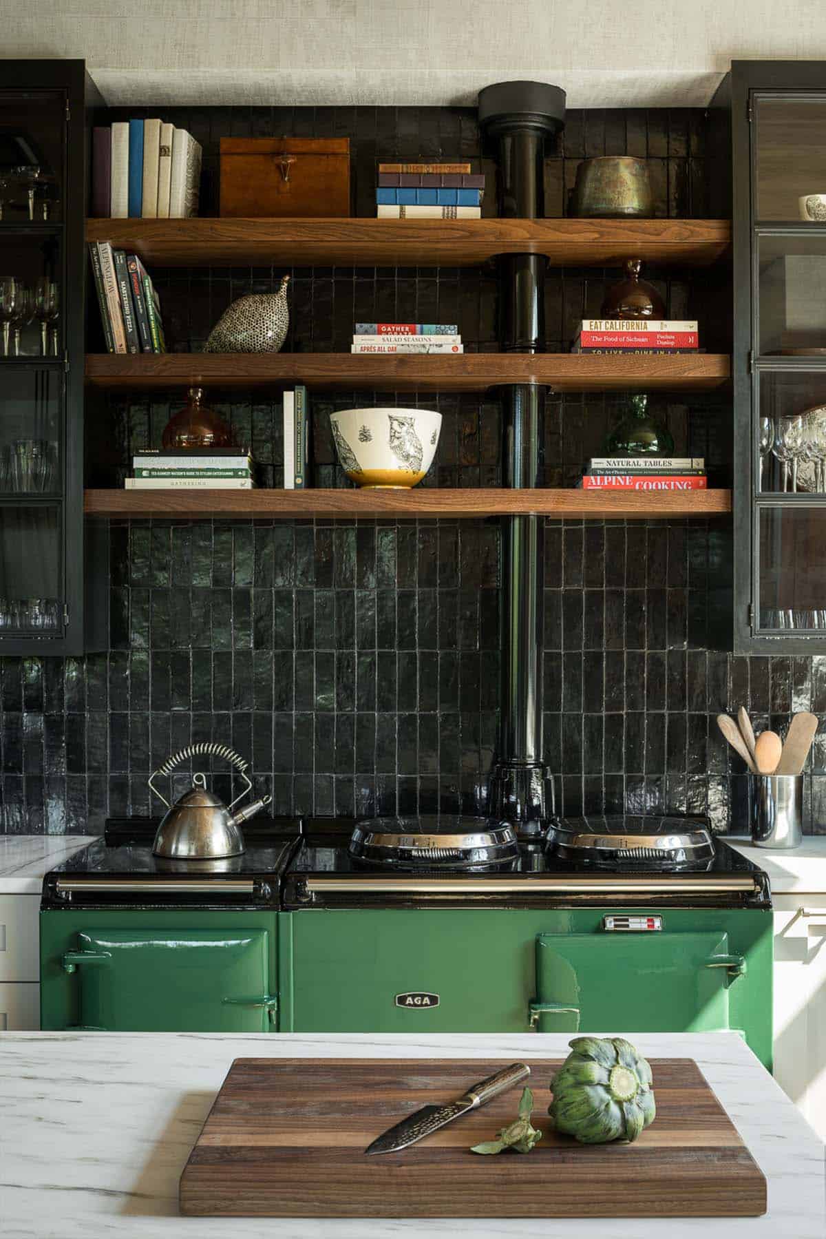 Green AGA range below walnut open shelves and glossy black tile