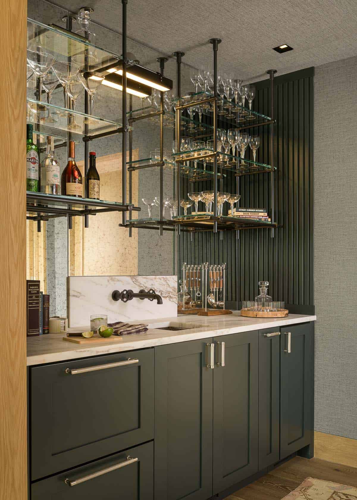 Home bar with green cabinetry and ceiling-hung glass shelves