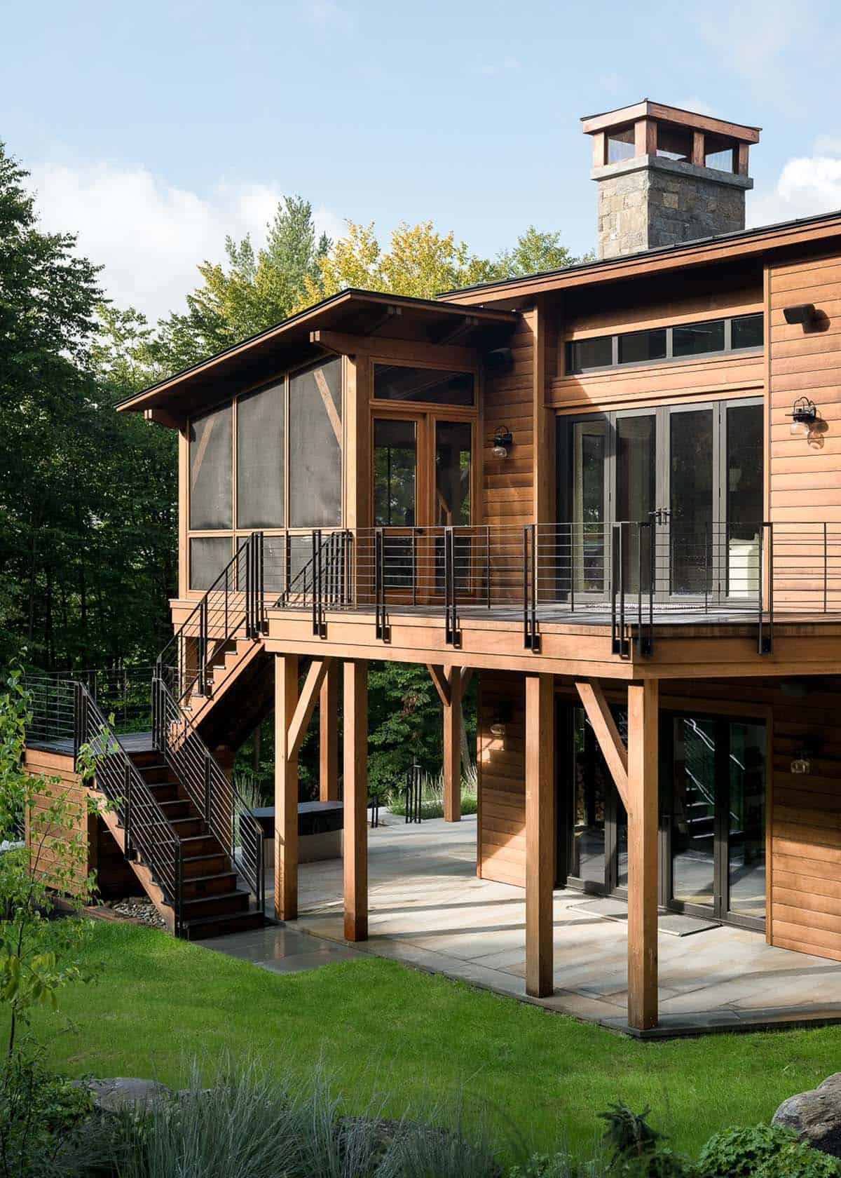 Rear exterior with cedar siding, upper deck, and stone patio below