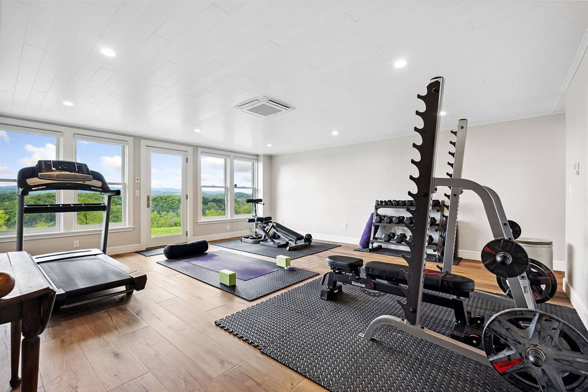 Home gym with a treadmill, squat rack, and weights by windows and a door looking out to the mountains