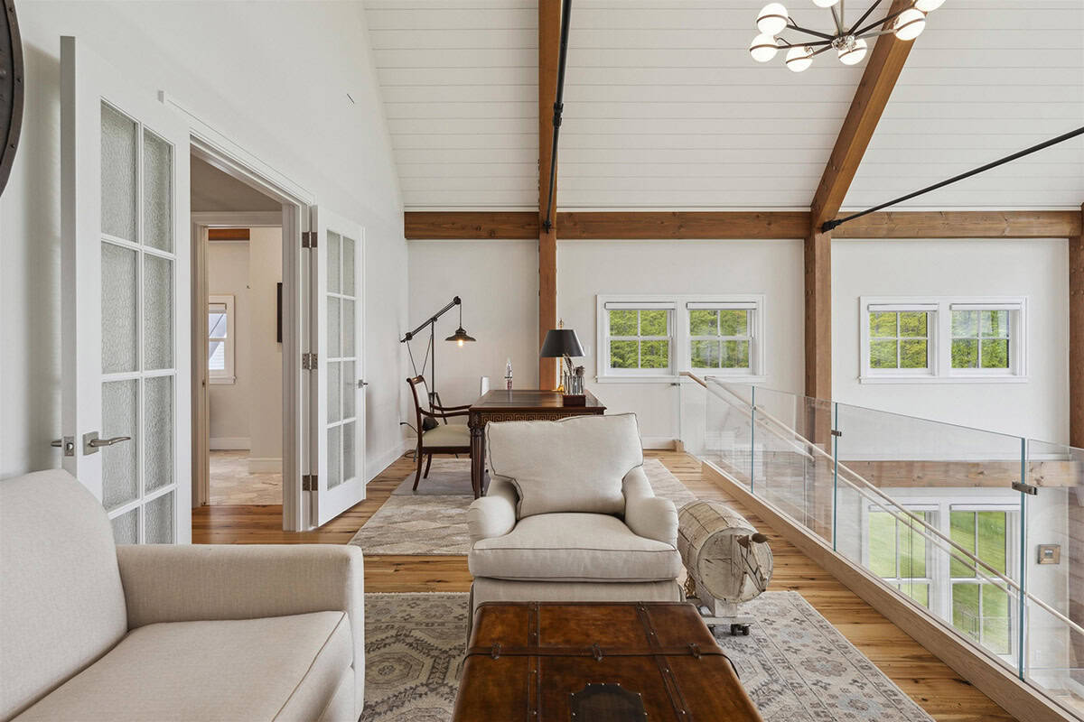 Loft sitting area and desk under timber beams, with a glass railing overlooking the great room
