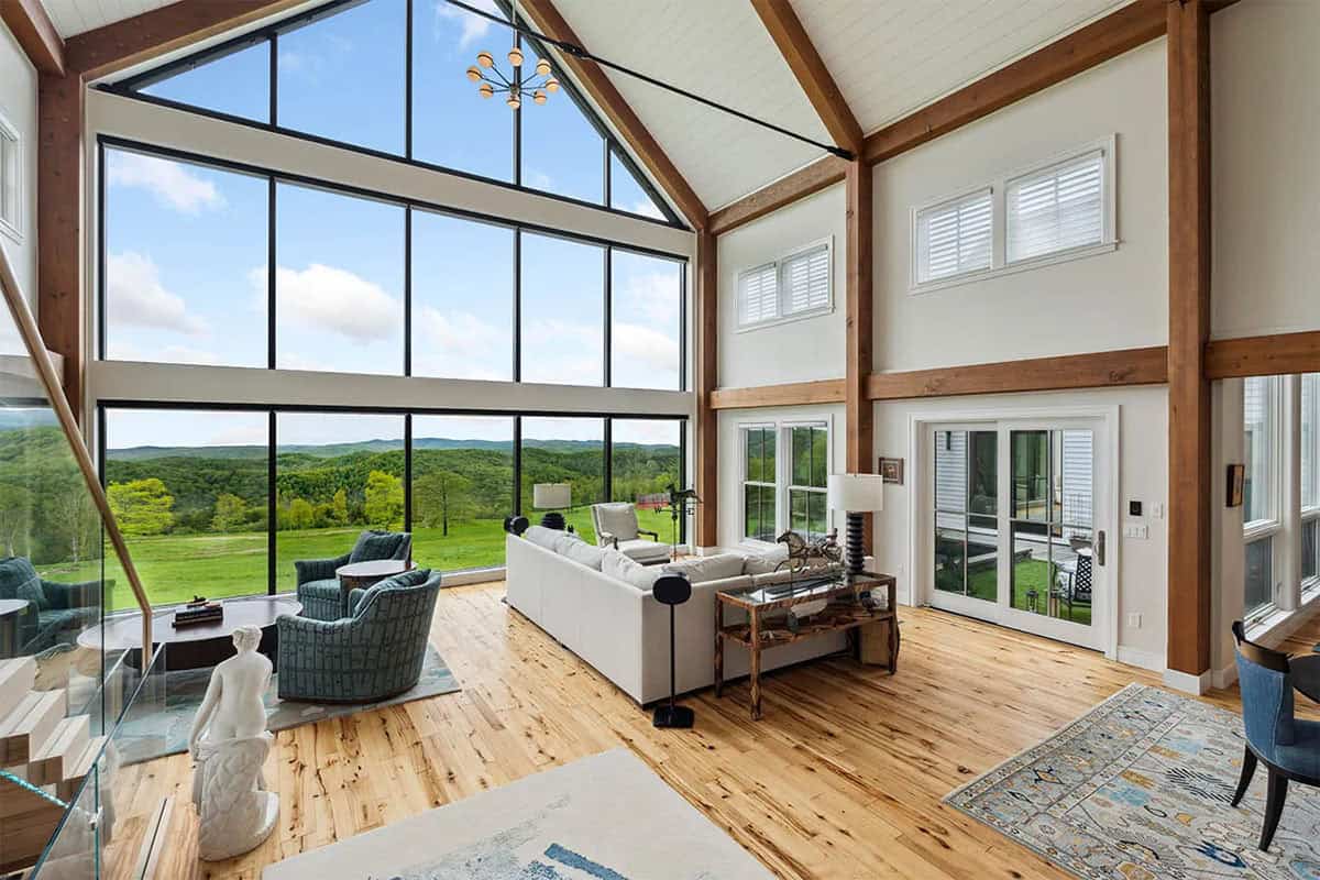 Great room with blue-green swivel chairs and a white sectional facing a glass gable wall with pasture and mountain views