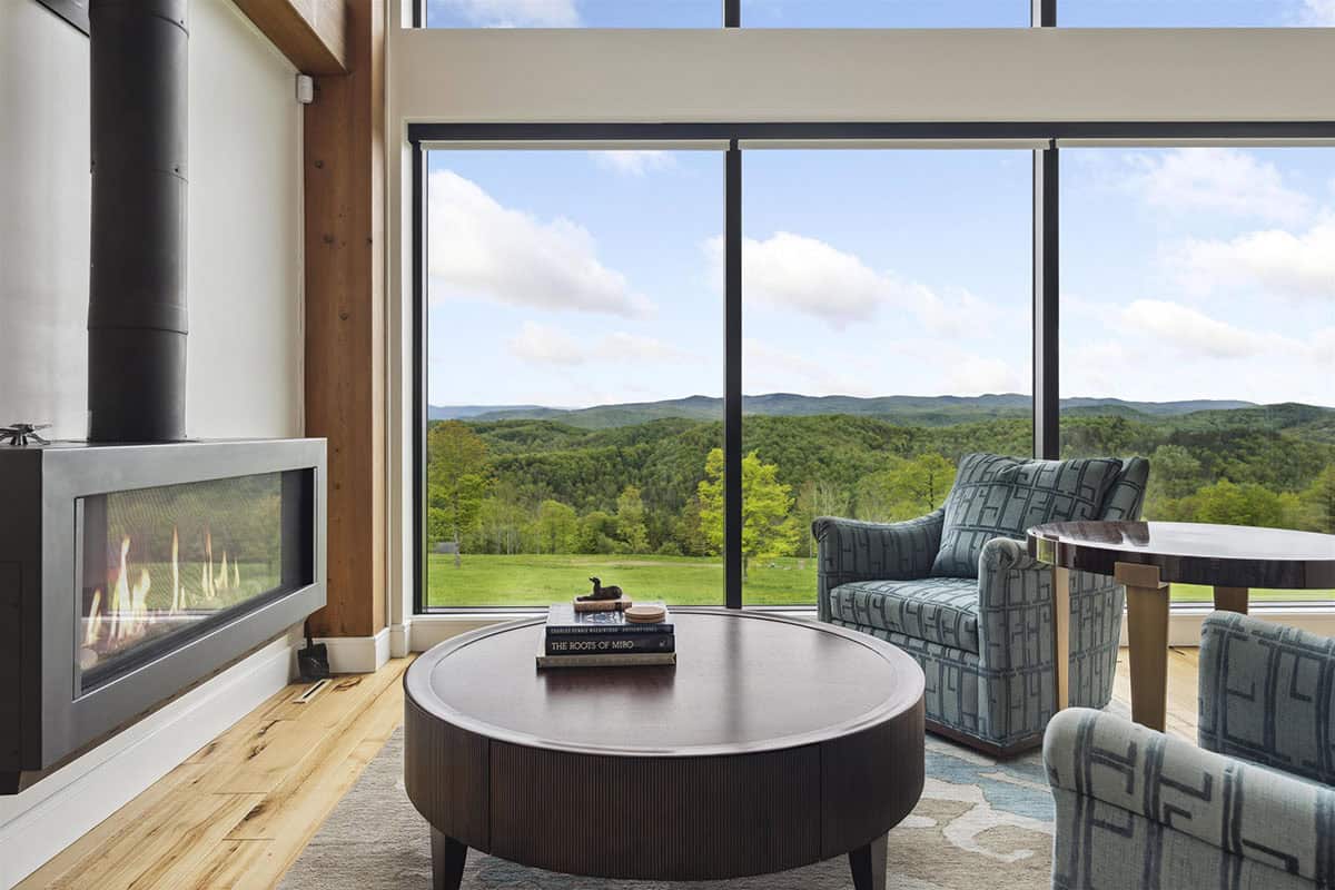 Linear gas fireplace beside a window wall with mountain views, a round wood coffee table, and a patterned armchair
