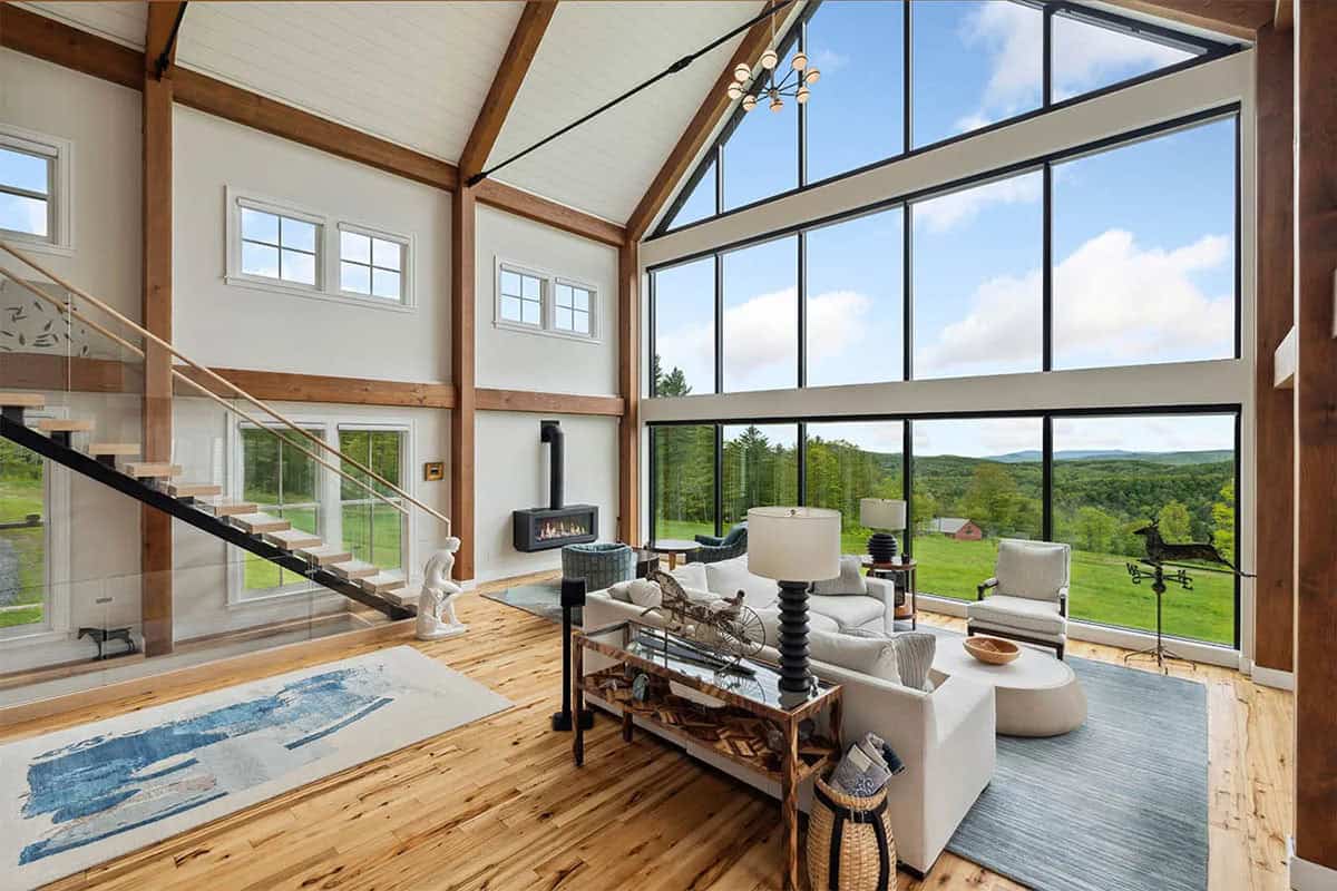Great room with a floating oak staircase, glass railing, wall-mounted fireplace, and floor-to-ceiling windows