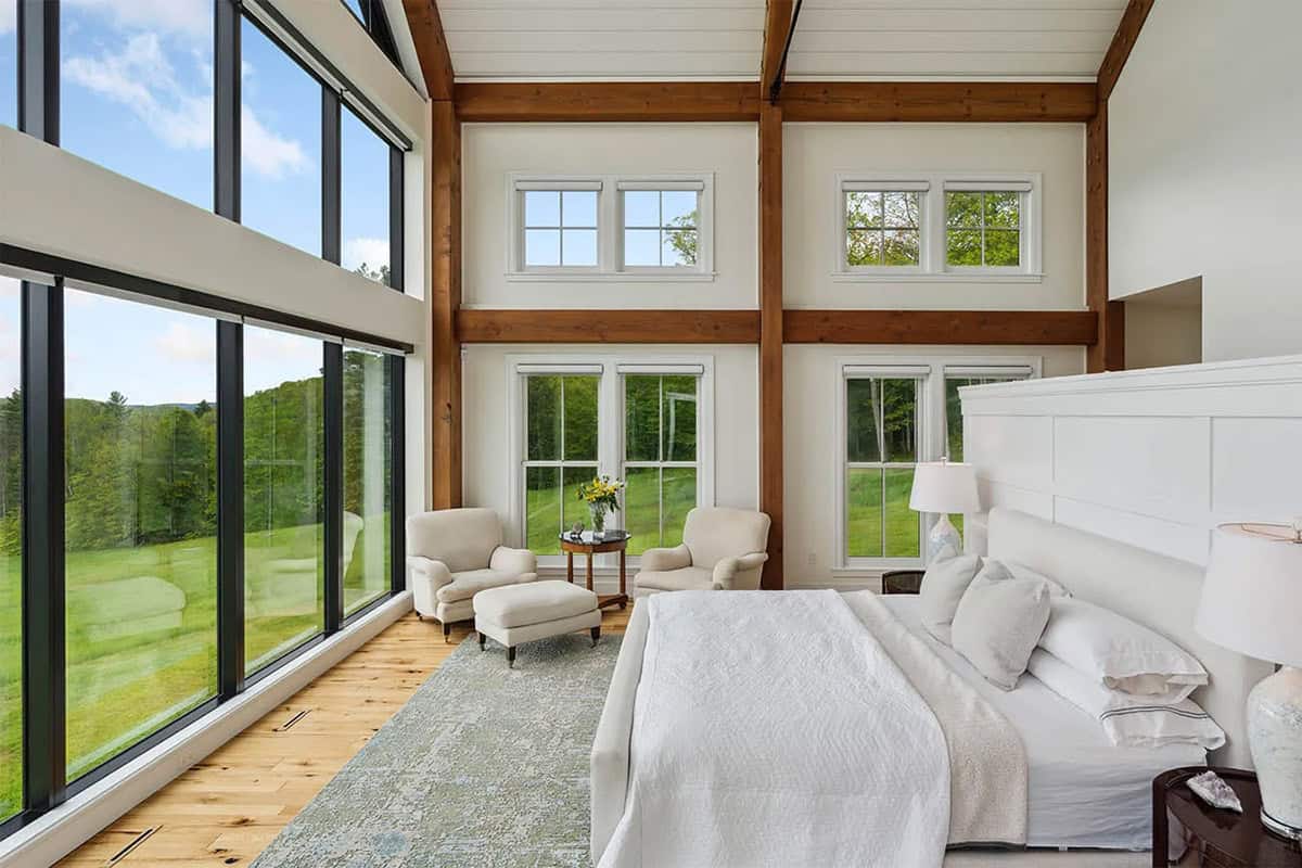 Primary bedroom with a window wall, timber posts, and a sitting area with two armchairs and an ottoman