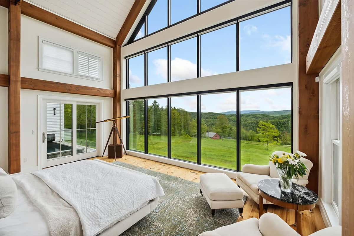 Primary bedroom with a glass gable wall overlooking a meadow and red barn, and a brass telescope by the courtyard door