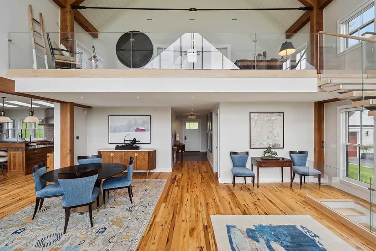 Dining area beneath a glass-railed loft, with a hallway leading to the front door