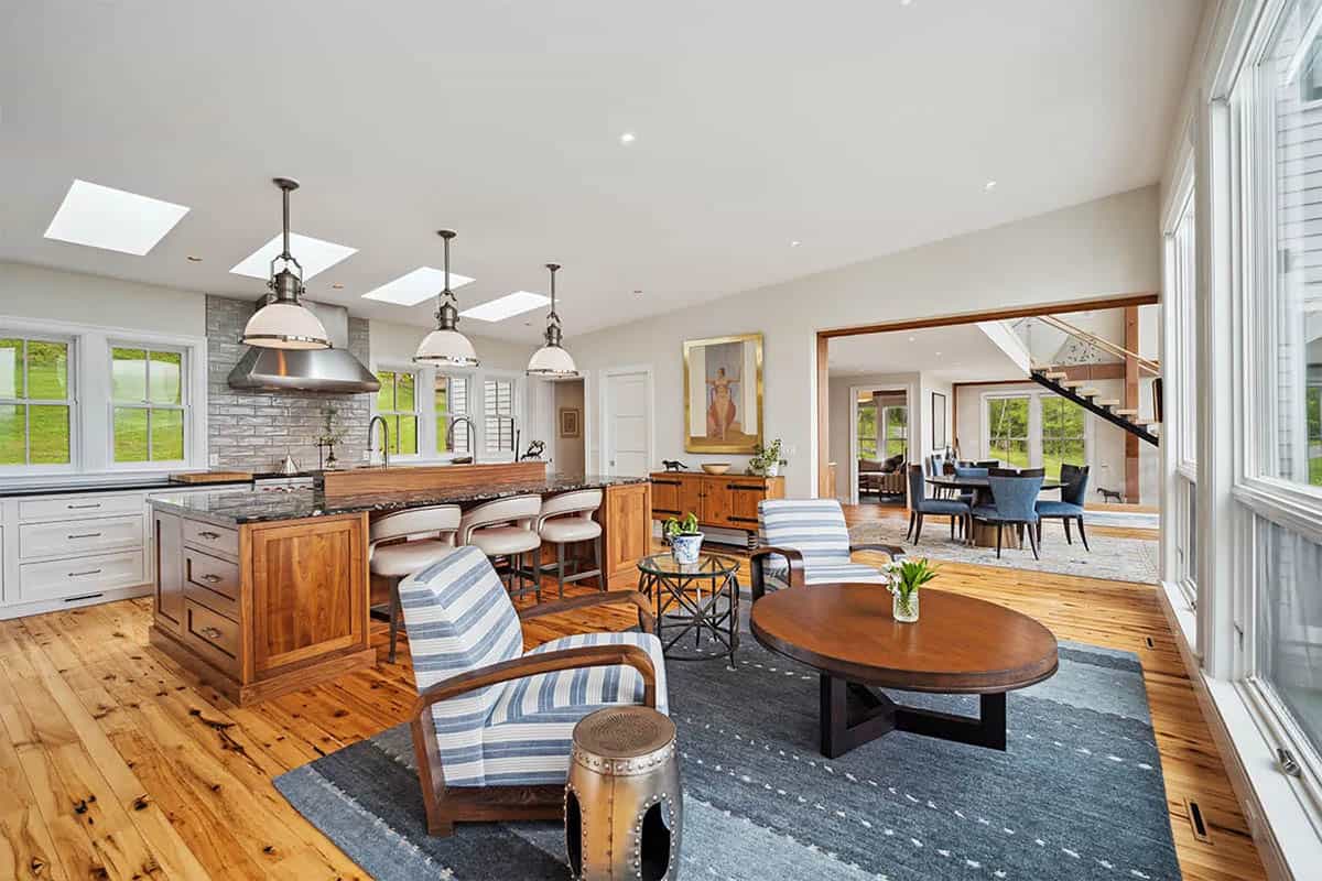 Kitchen with a walnut island, granite countertop, skylights, and enamel pendants, next to a sitting area with striped armchairs