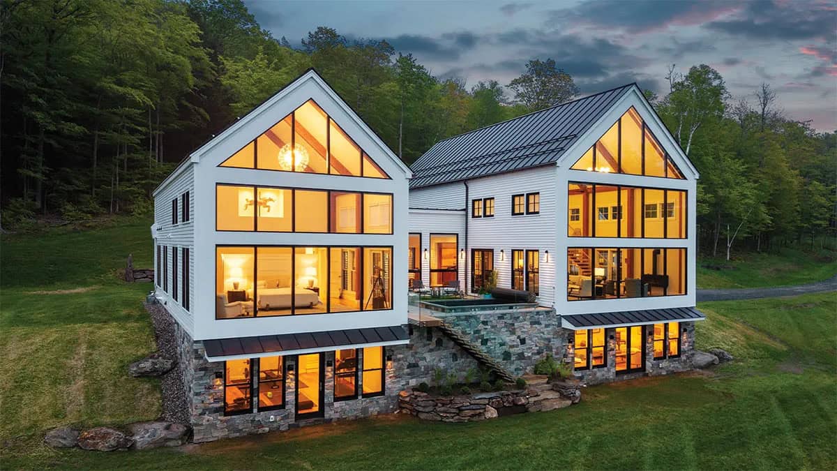 Farmhouse with two lit glass gables, a stone walkout level, and a courtyard pool at dusk