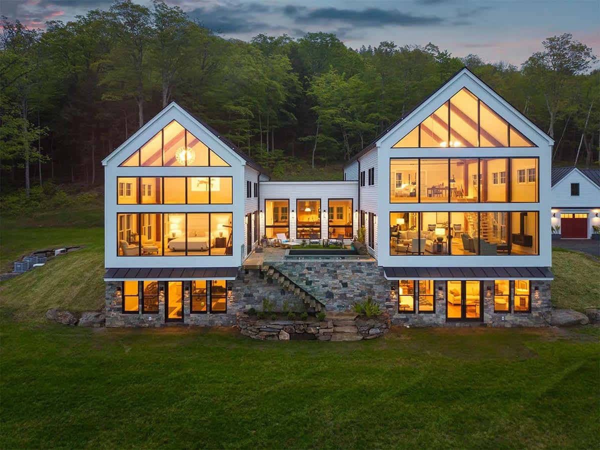 U-shaped farmhouse at dusk with glowing glass gables on either side of a courtyard pool and stone staircase
