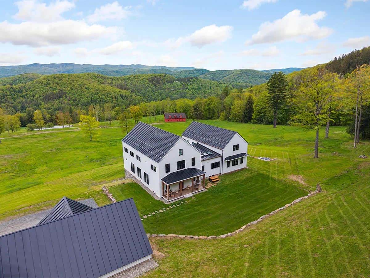 Aerial view of the farmhouse in an open meadow with a red barn and rolling Vermont mountains