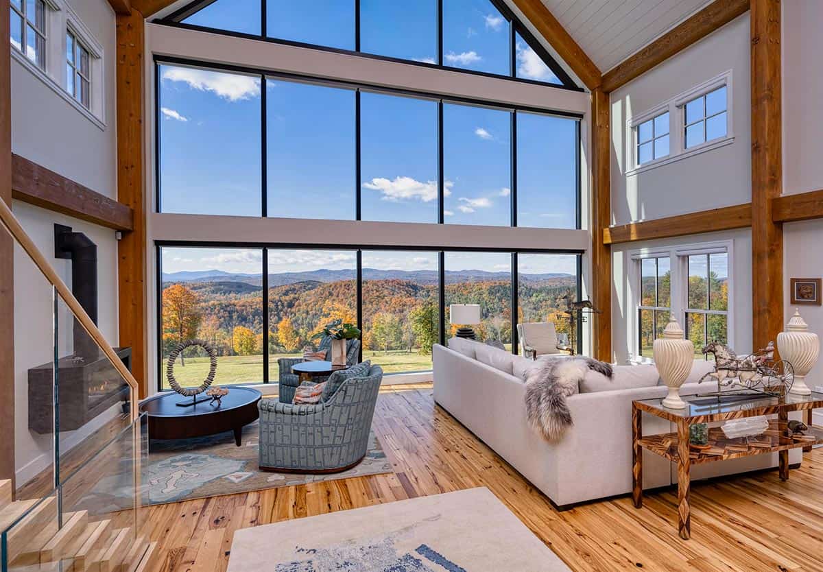Timber frame great room with a two-story glass gable wall framing fall foliage across the Vermont hills