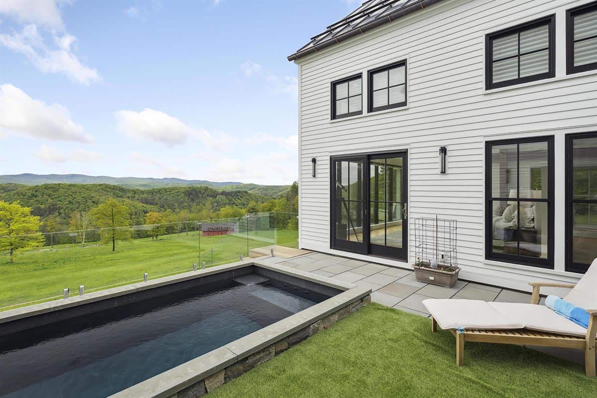 Heated plunge pool in the raised courtyard with a glass railing overlooking the meadow, red barn, and mountains