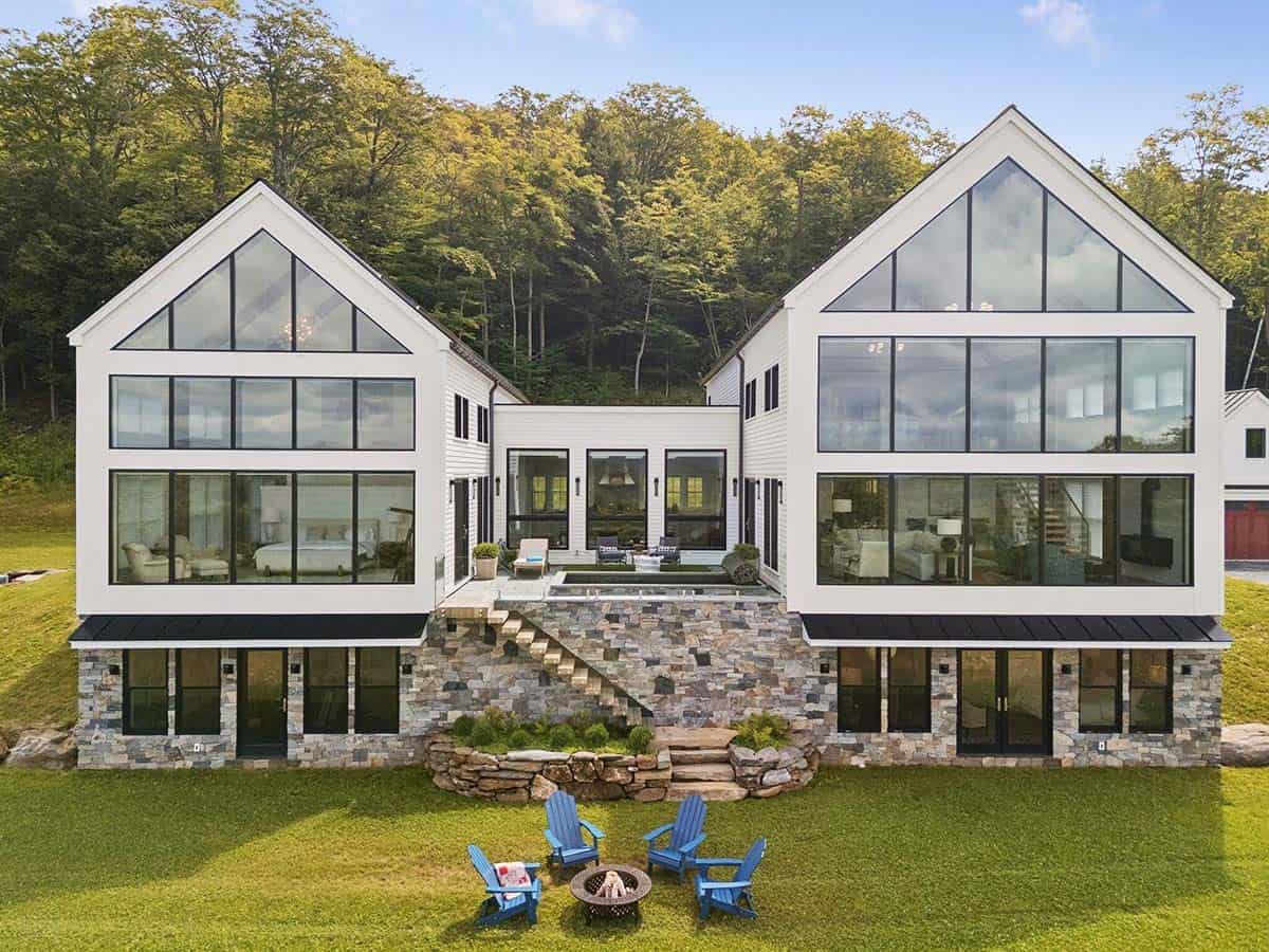 Rear of the farmhouse in daylight with two glass gables, a stone staircase from the courtyard, and blue Adirondack chairs around a fire pit