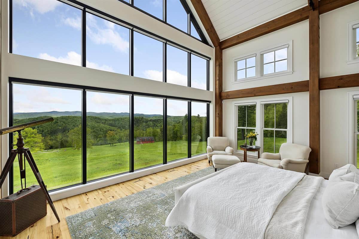 Owner's bedroom with a glass gable wall overlooking a meadow and red barn, with a brass telescope on a tripod