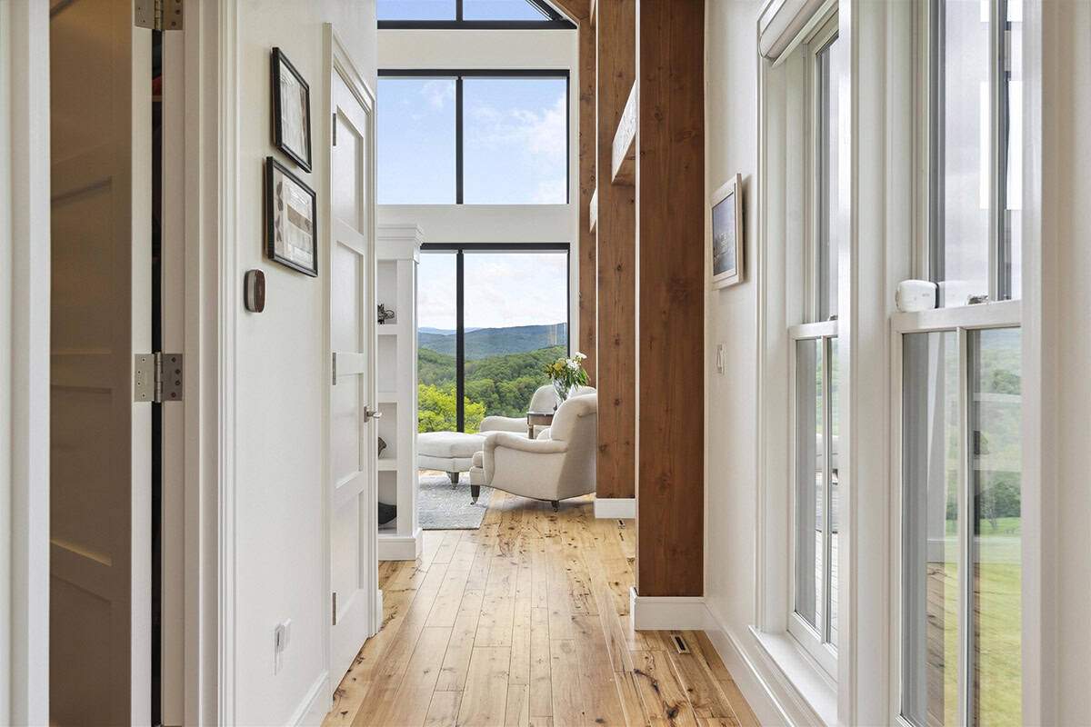 Hallway with exposed timber posts and tall windows leading to the owner's bedroom sitting area and mountain views