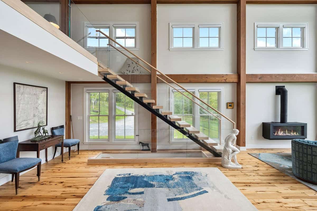 Floating oak staircase with a black steel stringer and glass railing, next to a wall-mounted gas fireplace