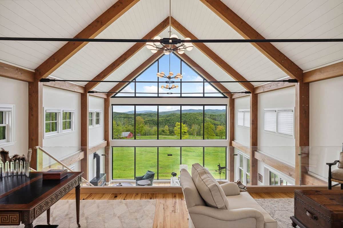 View from the loft across the timber frame great room to a glass gable wall overlooking the meadow and red barn