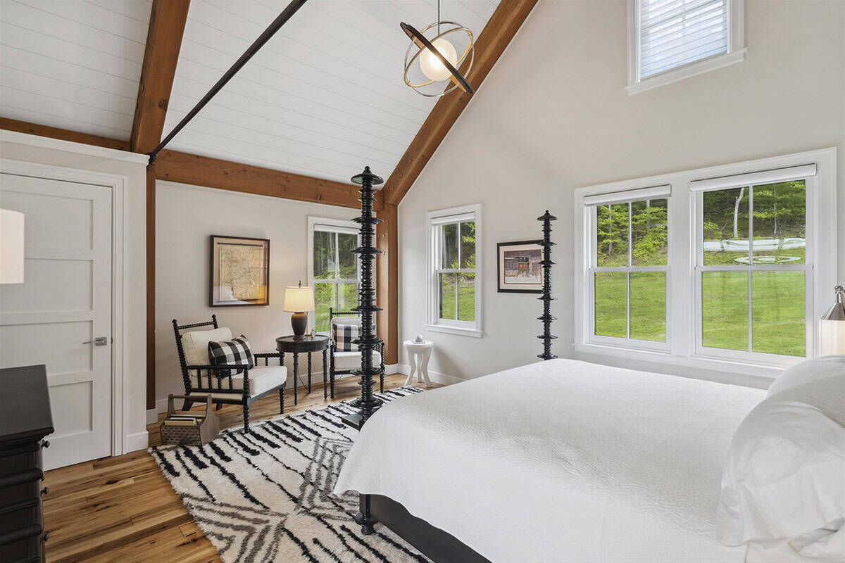 Guest bedroom with a black spindle four-poster bed, vaulted ceiling with timber beams, and a black and white rug