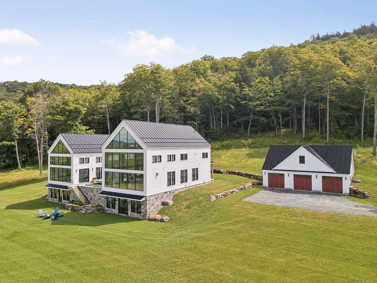 Aerial view of the farmhouse with glass gables and a stone walkout level beside a three-bay garage with red doors