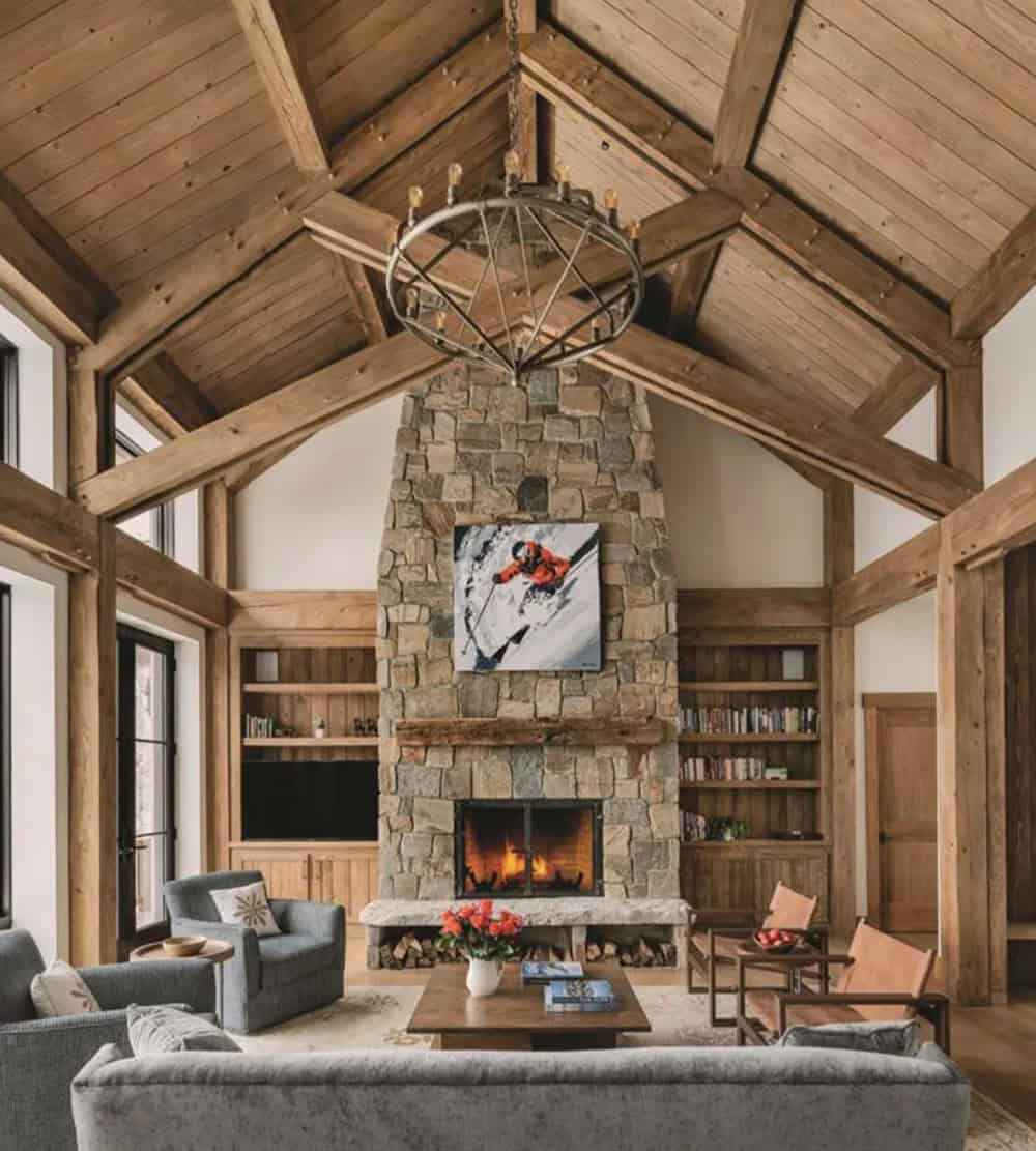 Vaulted great room with a timber-framed ceiling, a wrought-iron ring chandelier and a stone fireplace with a skier painting flanked by built-in shelves