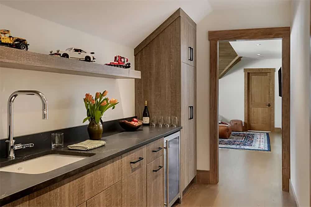 Upstairs kitchenette with gray oak cabinets, a black countertop, a wine refrigerator and a floating shelf of toy vehicles