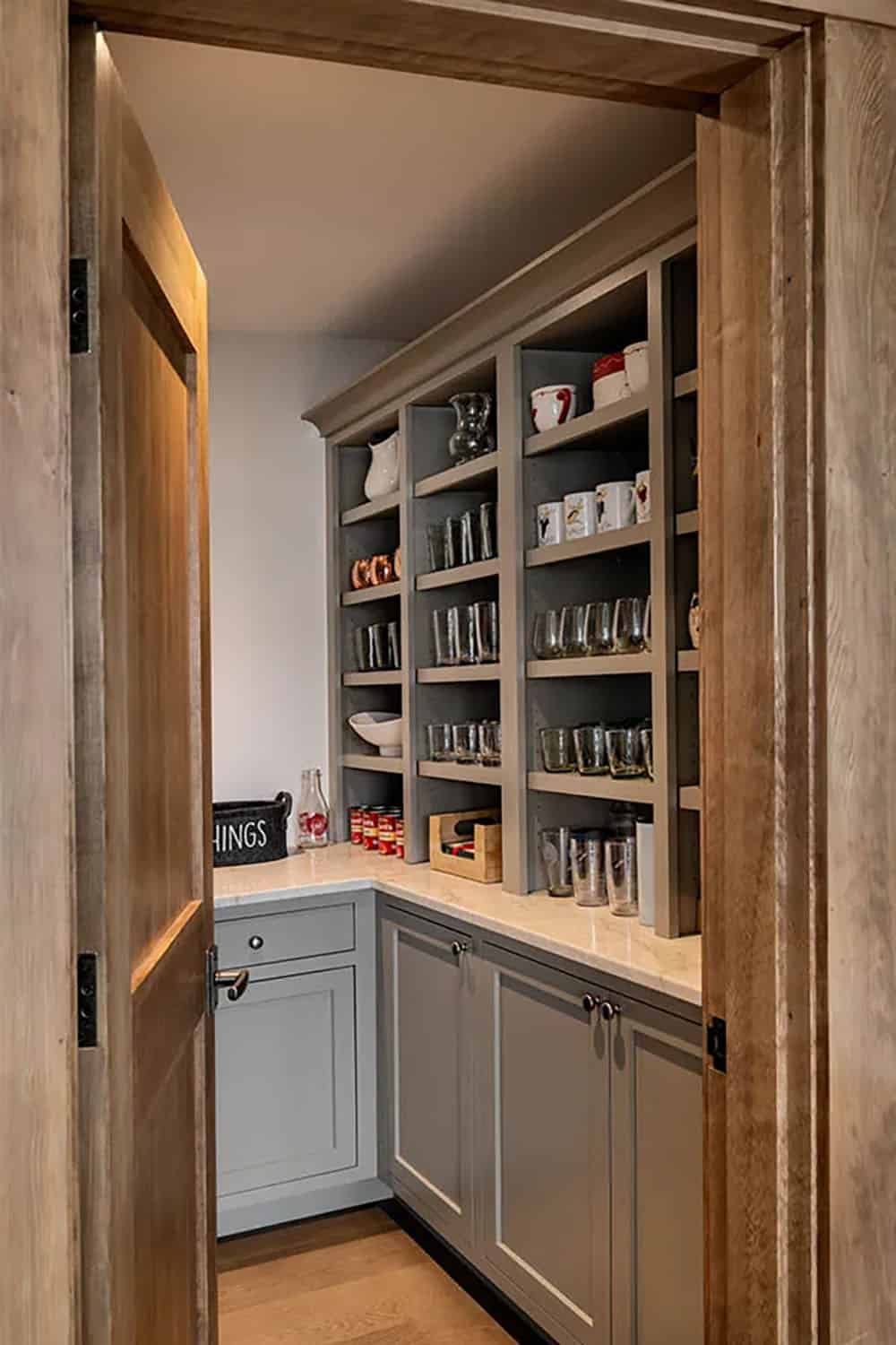 Walk-in pantry with gray cabinets, open shelves of glassware and mugs and a marble countertop