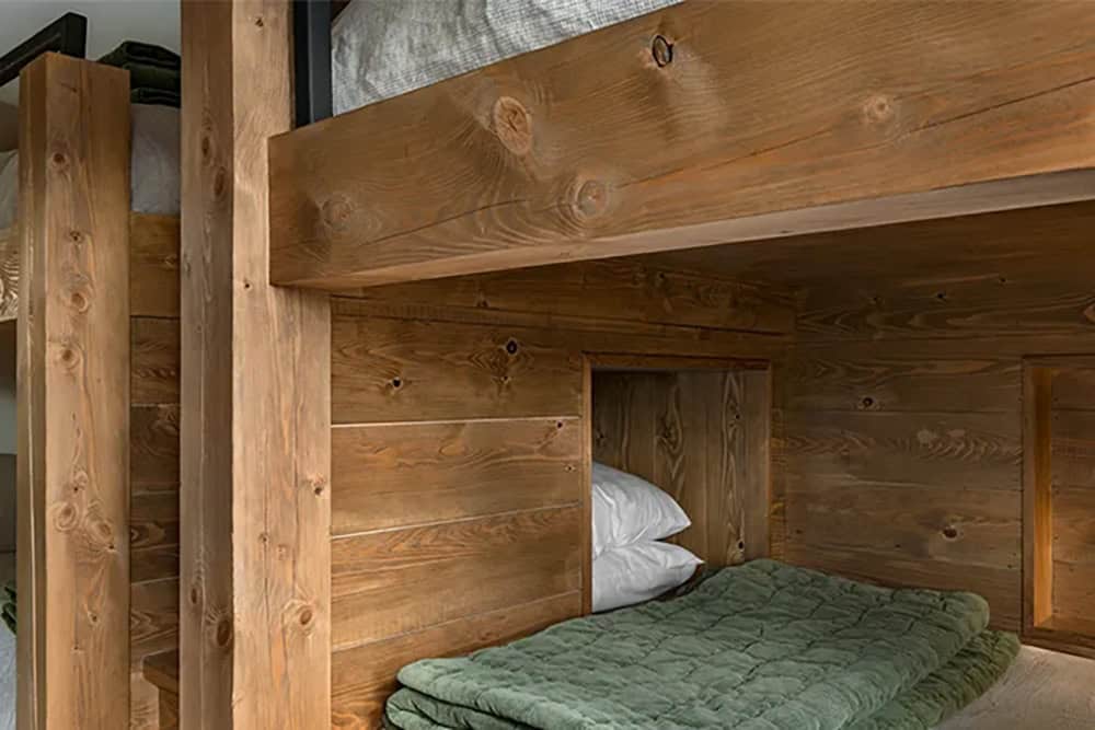 Close-up of rough-hewn timber bunk beds with a built-in wall nook beside a lower bunk