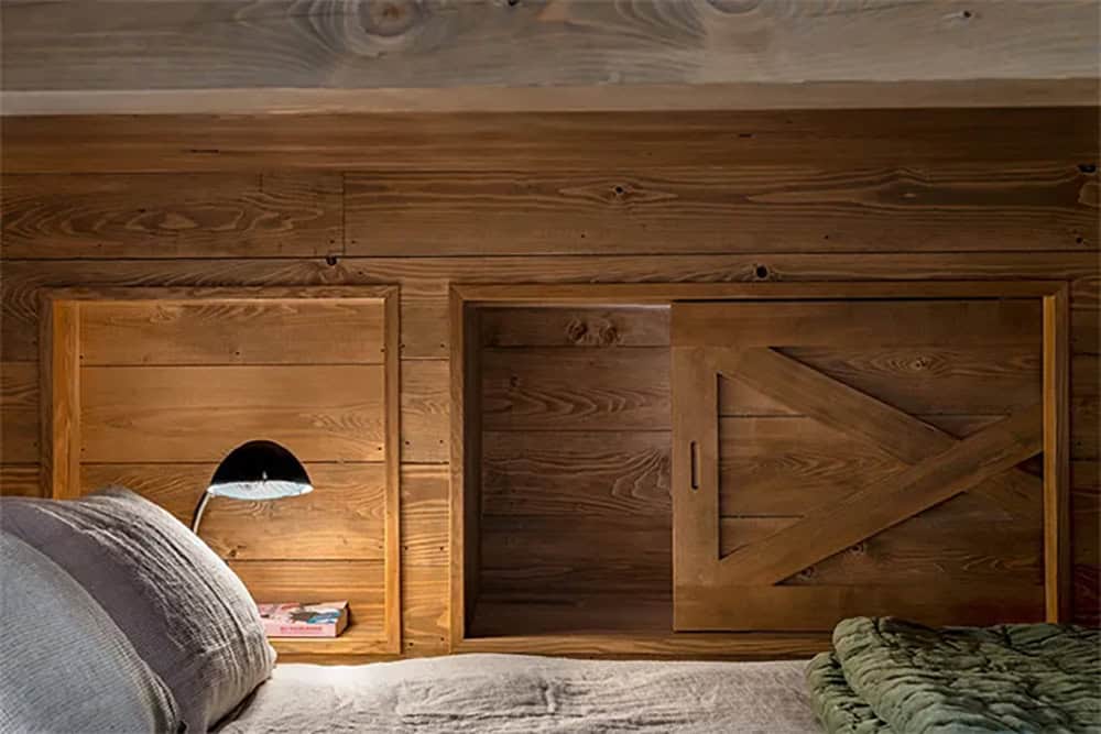 Built-in wall niches above a bunk bed, one with a reading lamp and the other with a sliding Z-brace wood door