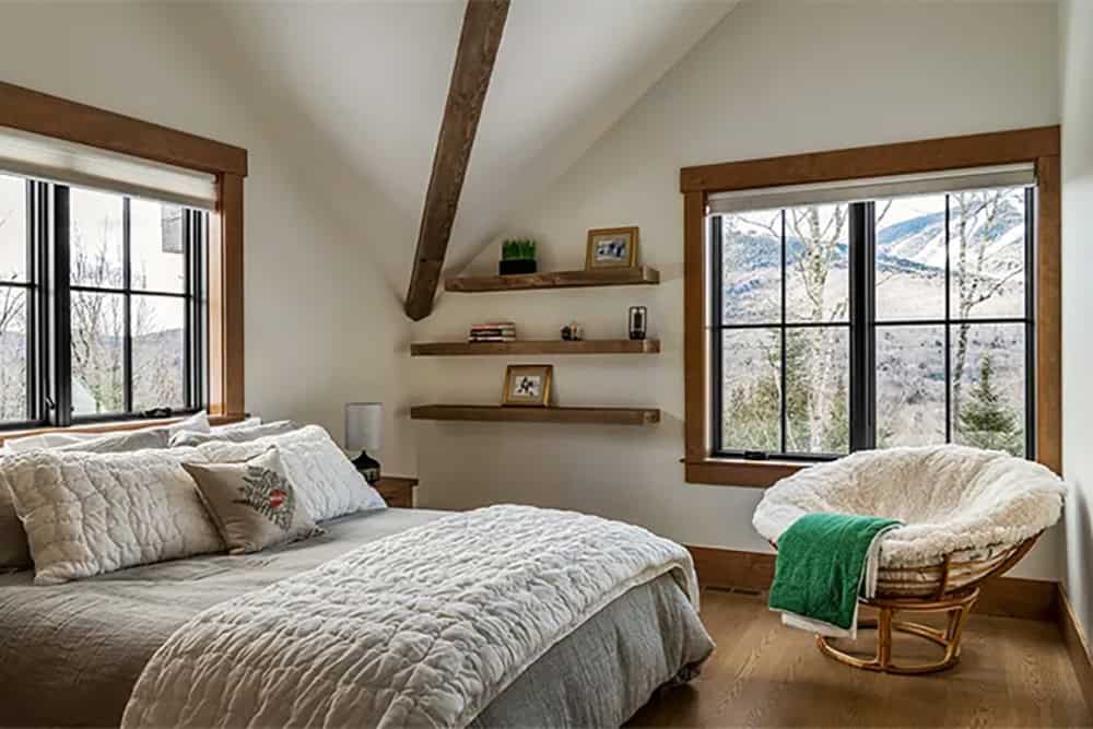 Bedroom with a sloped ceiling and exposed beam, floating wood shelves, a fur papasan chair and windows overlooking snowy mountains