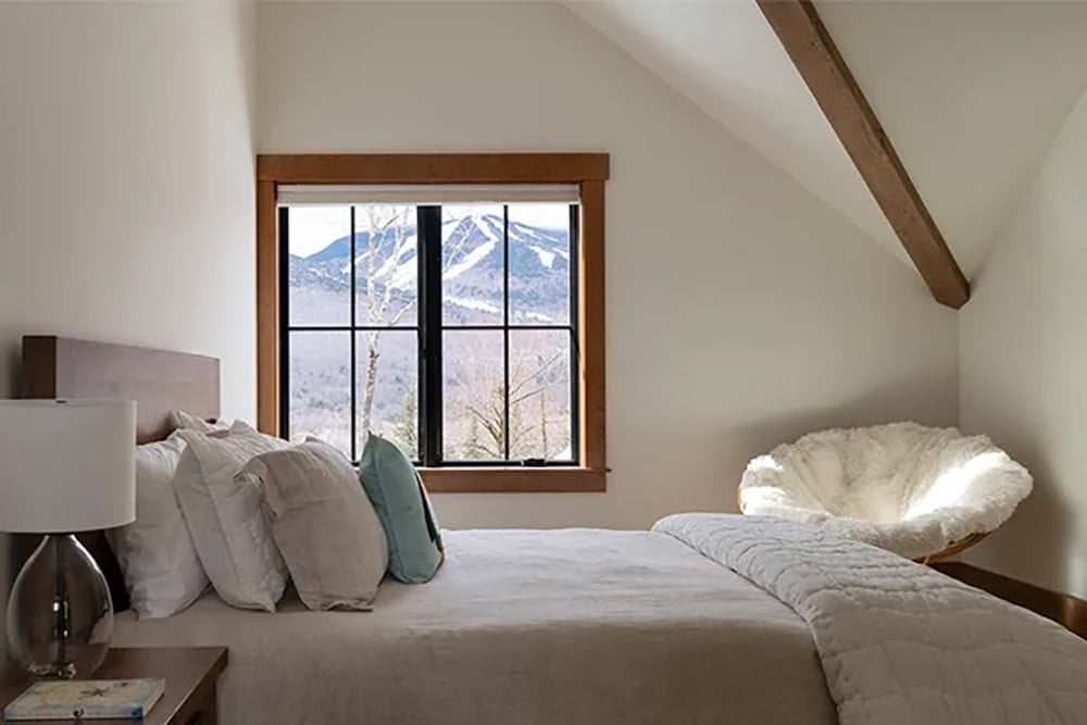 Bedroom with a window framing ski trails on a snow-covered mountain, a fur papasan chair and an exposed ceiling beam