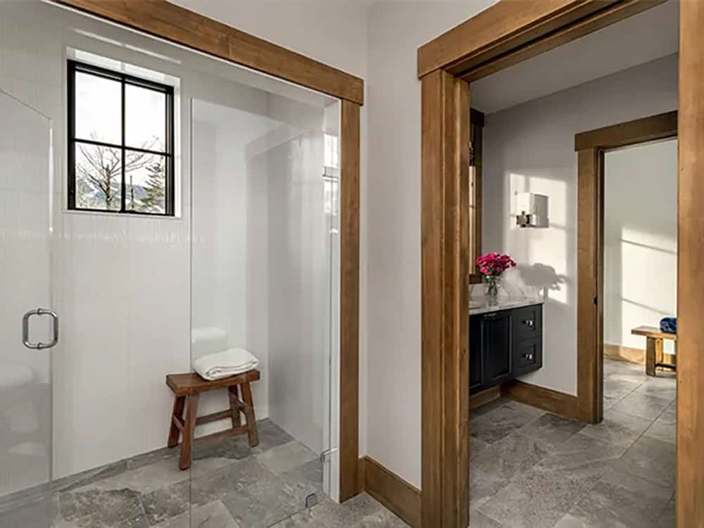 Bathroom with a glass walk-in shower and teak stool beside a doorway leading to a navy vanity with a marble countertop