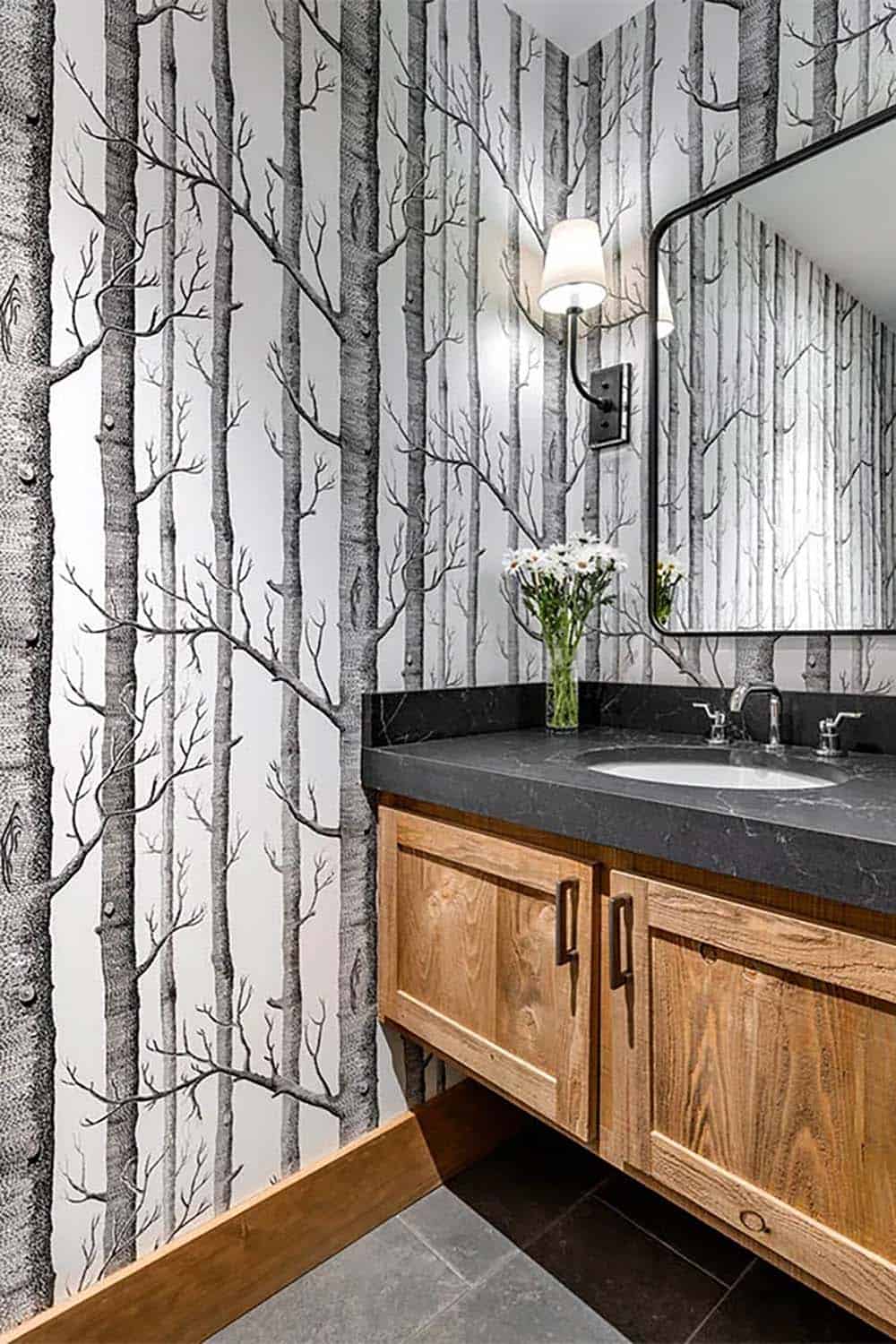 Powder room with black-and-white birch tree wallpaper, a wood vanity with a black stone countertop and a black-framed mirror