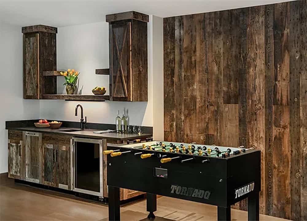 Lower-level wet bar with reclaimed barn wood cabinets and wall paneling, a beverage refrigerator and a foosball table