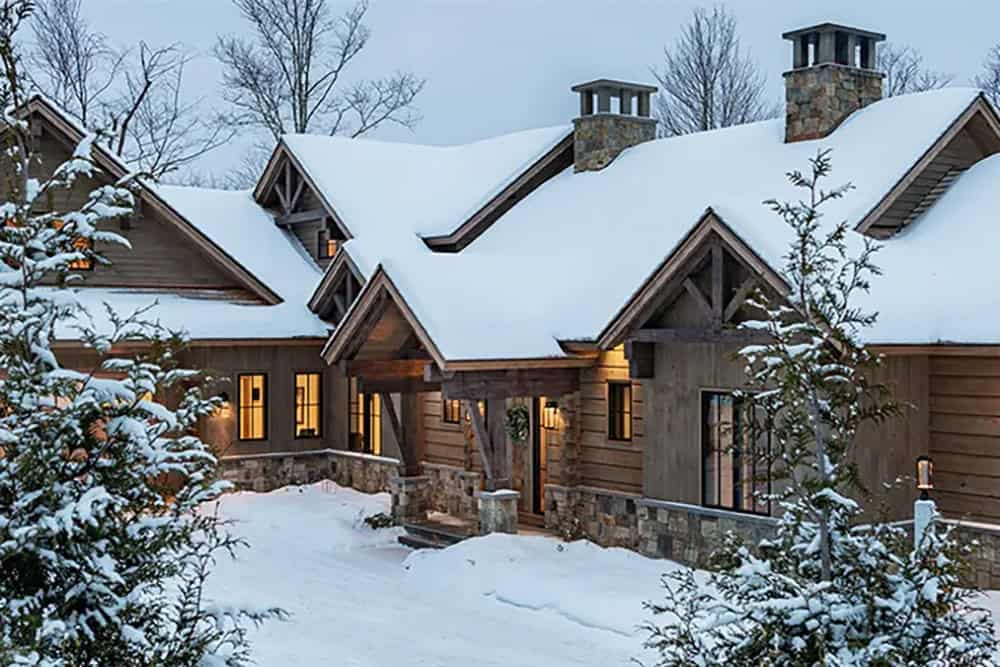 Snow-covered roofline and timber gable entry porch of a mountain home at twilight, framed by snowy evergreens