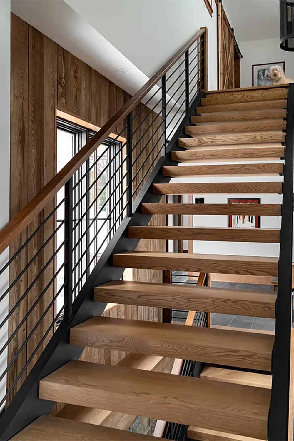 Open staircase with thick oak treads, a black steel stringer and horizontal rod railing beside a reclaimed wood wall