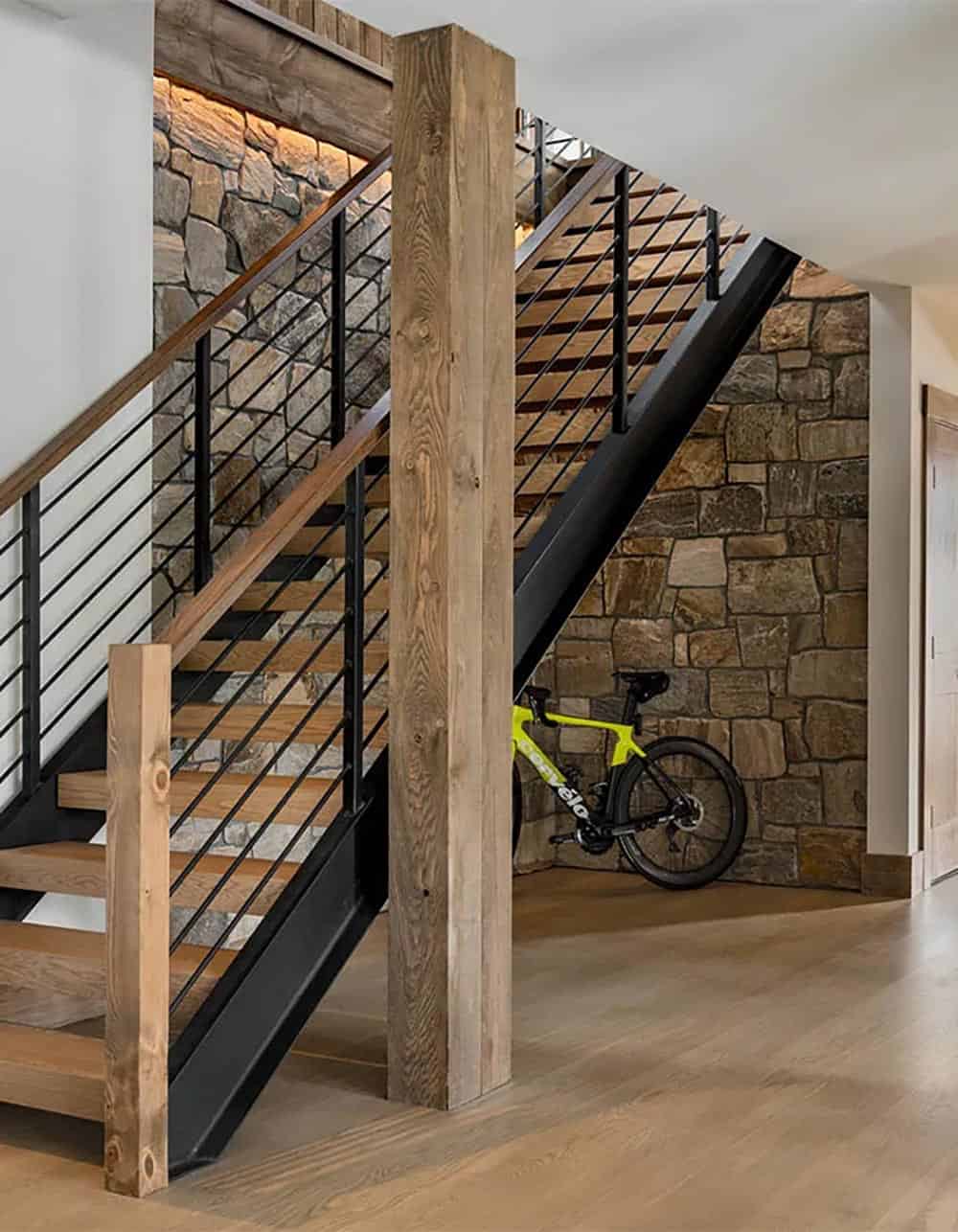 Floating oak staircase with black steel railing and a rough timber post against a stone wall, with a road bike parked beneath