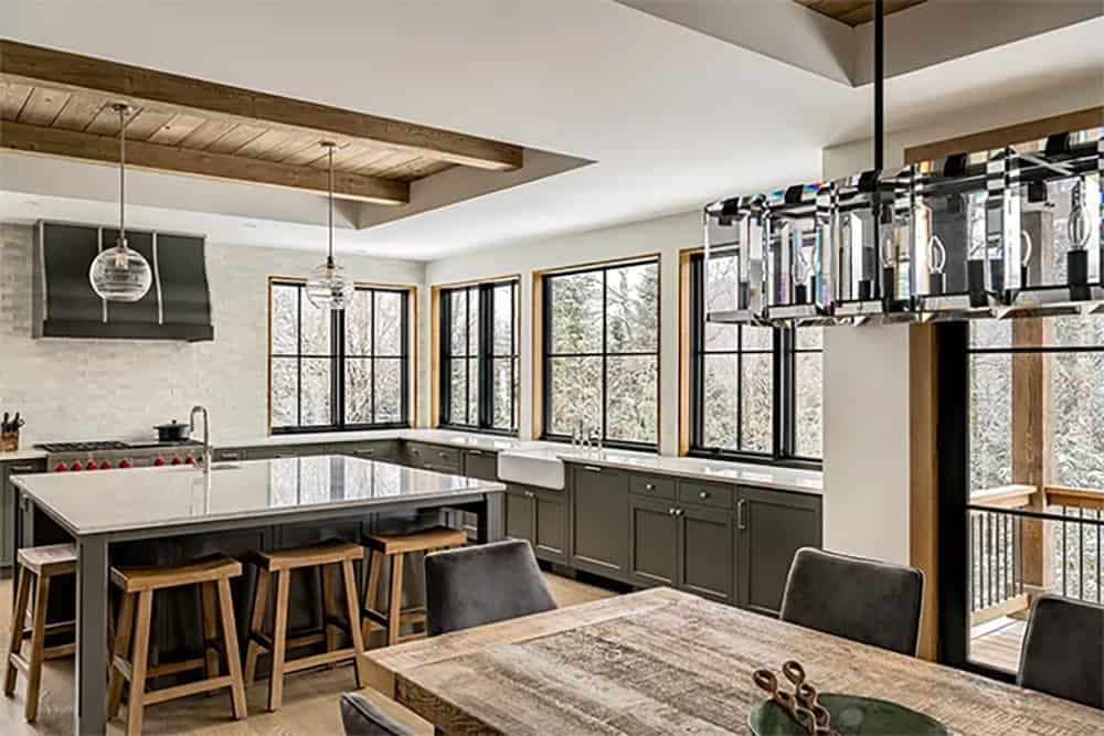 Kitchen with olive green cabinets, a large stone-topped island with wood stools, a black range hood and a crystal dining chandelier