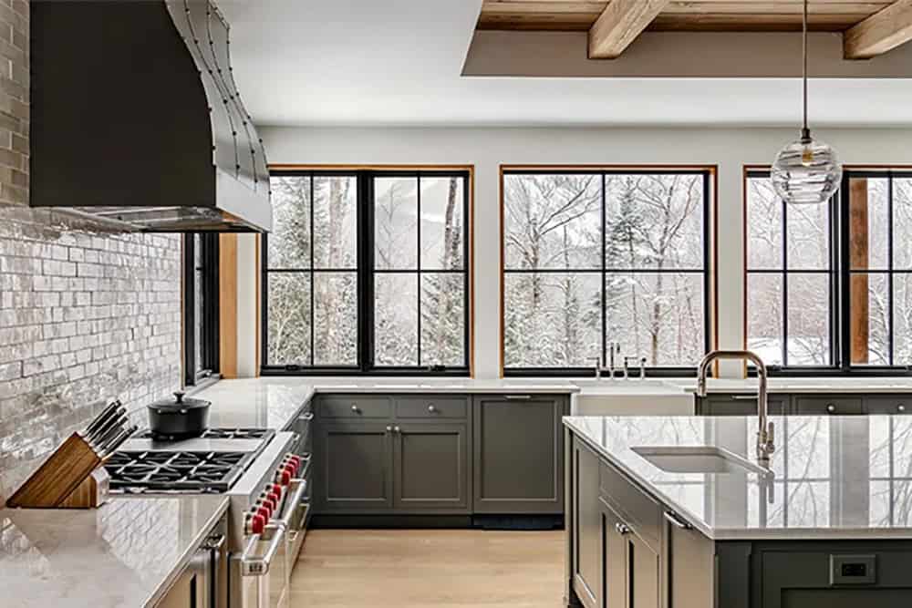 Kitchen corner with green Shaker cabinets, a farmhouse sink, a professional range under a black hood and walls of black-framed windows
