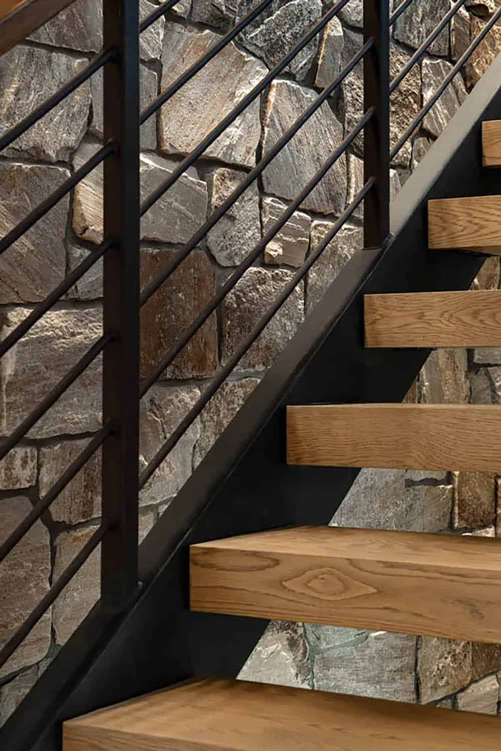 Close-up of floating oak stair treads on a black steel stringer against a fieldstone wall