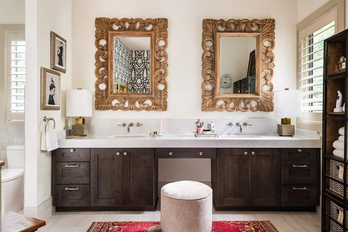Primary bathroom double vanity with carved wood mirrors and upholstered stool