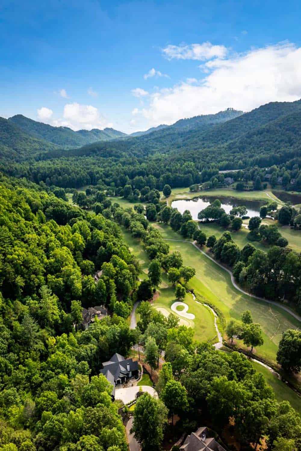 Aerial view of golf course, pond and mountains with home in the trees