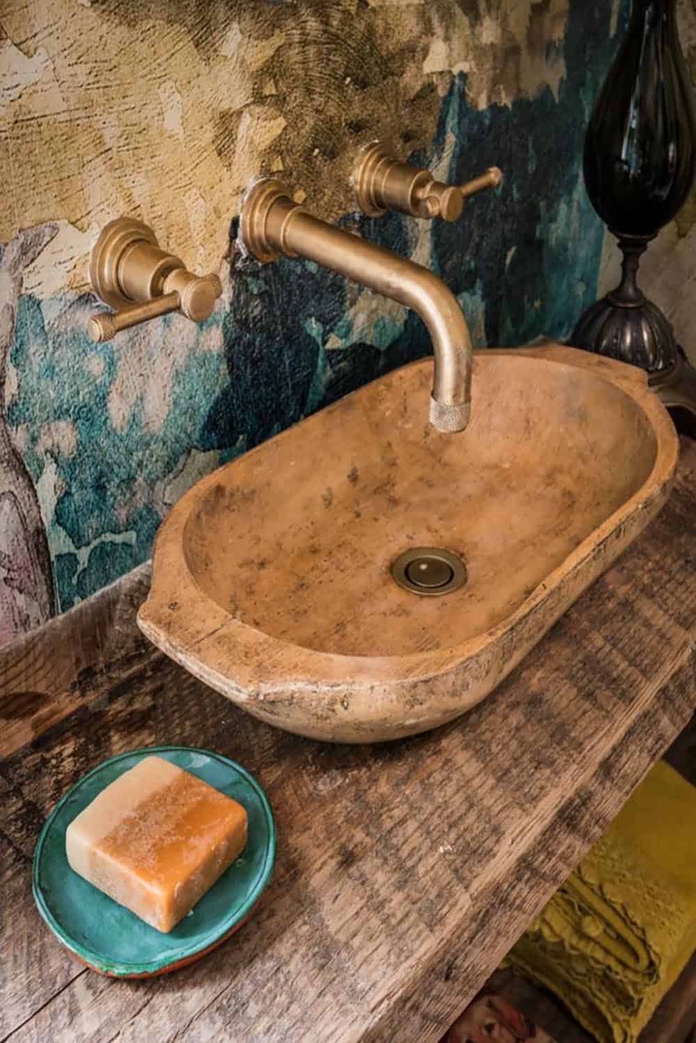 Close-up of wood bowl sink with brass wall faucet and green soap dish