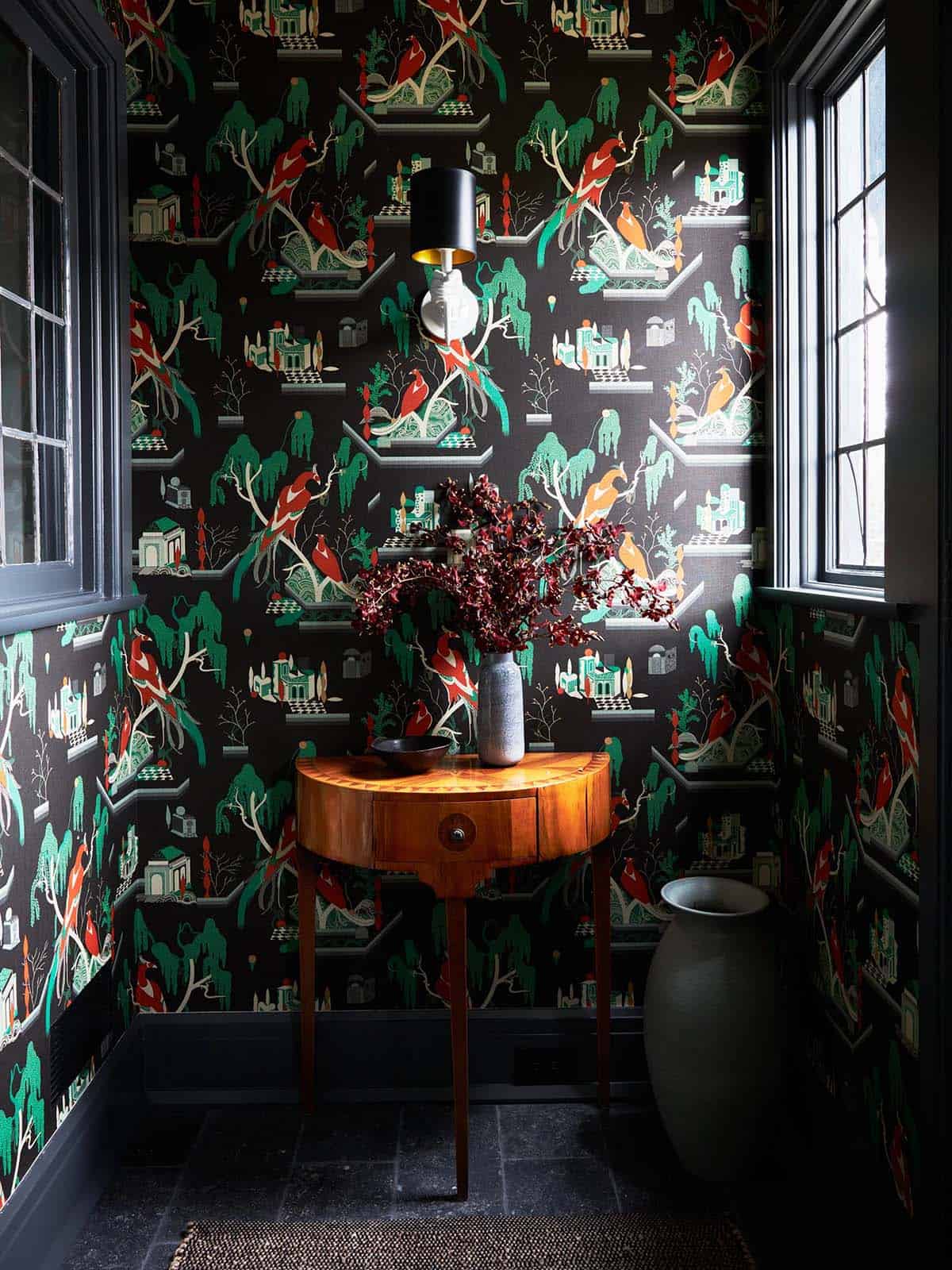 Entry nook with bird-patterned wallpaper, demilune table and hand sconce