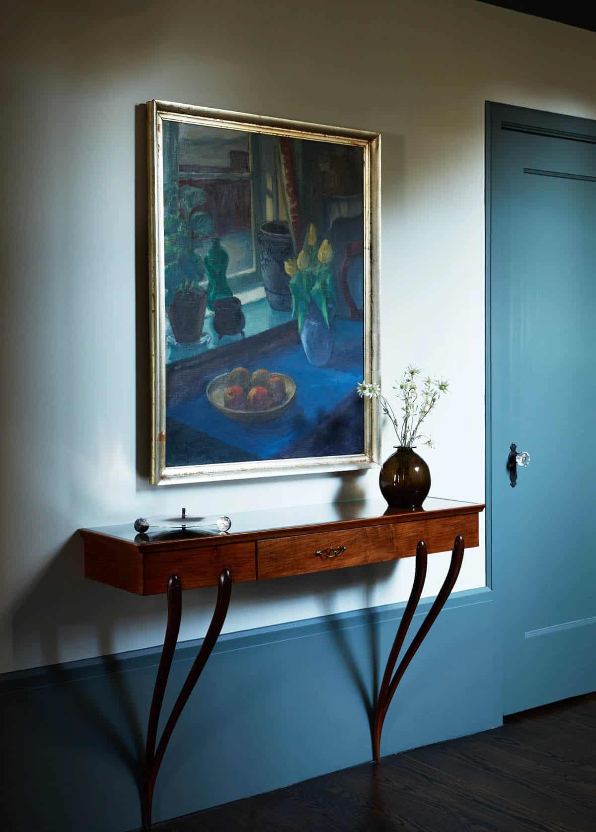 Wall-mounted walnut console beneath a blue still life painting