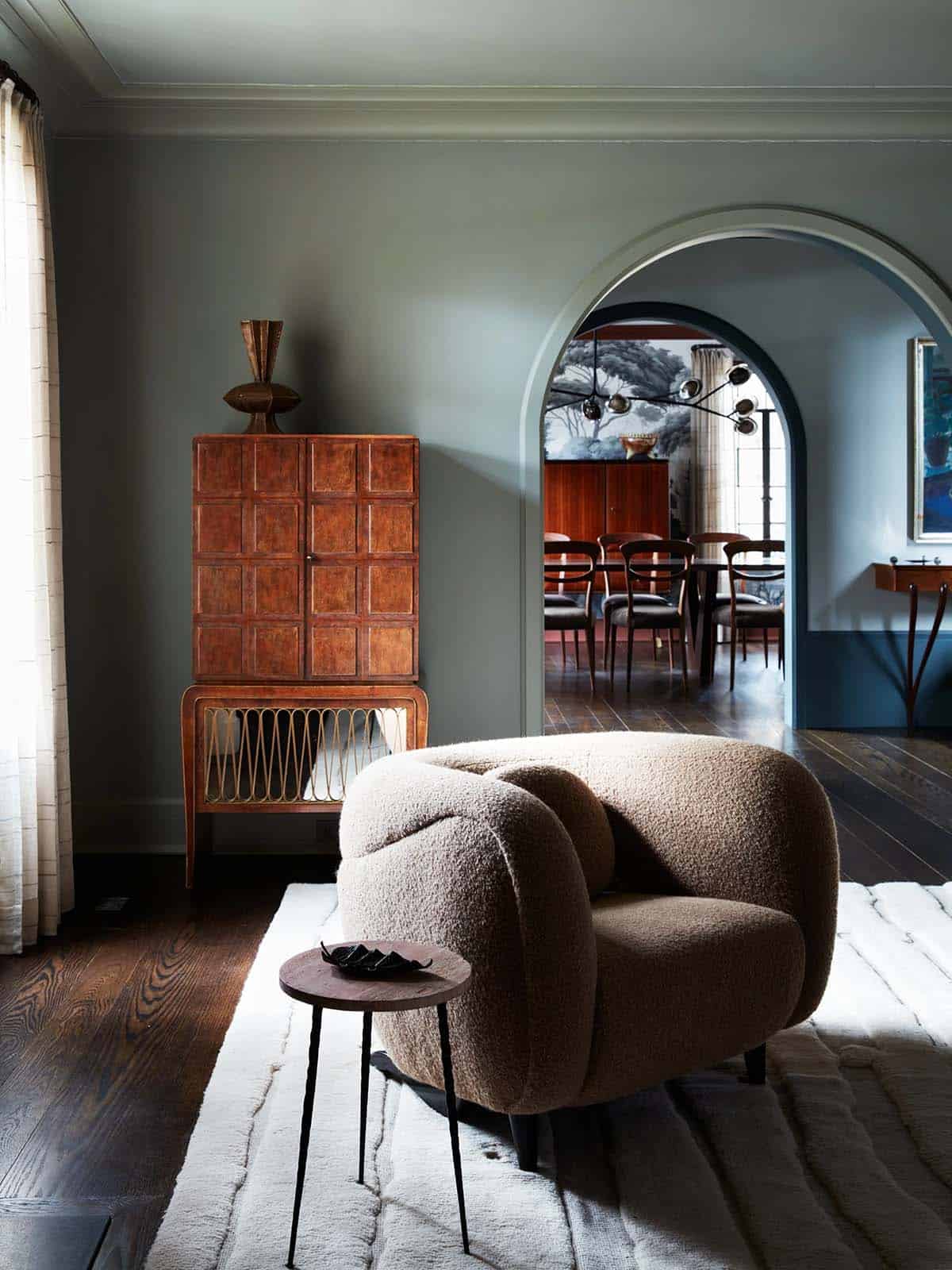 Bouclé armchair and parquetry cabinet beside arched doorway to dining room