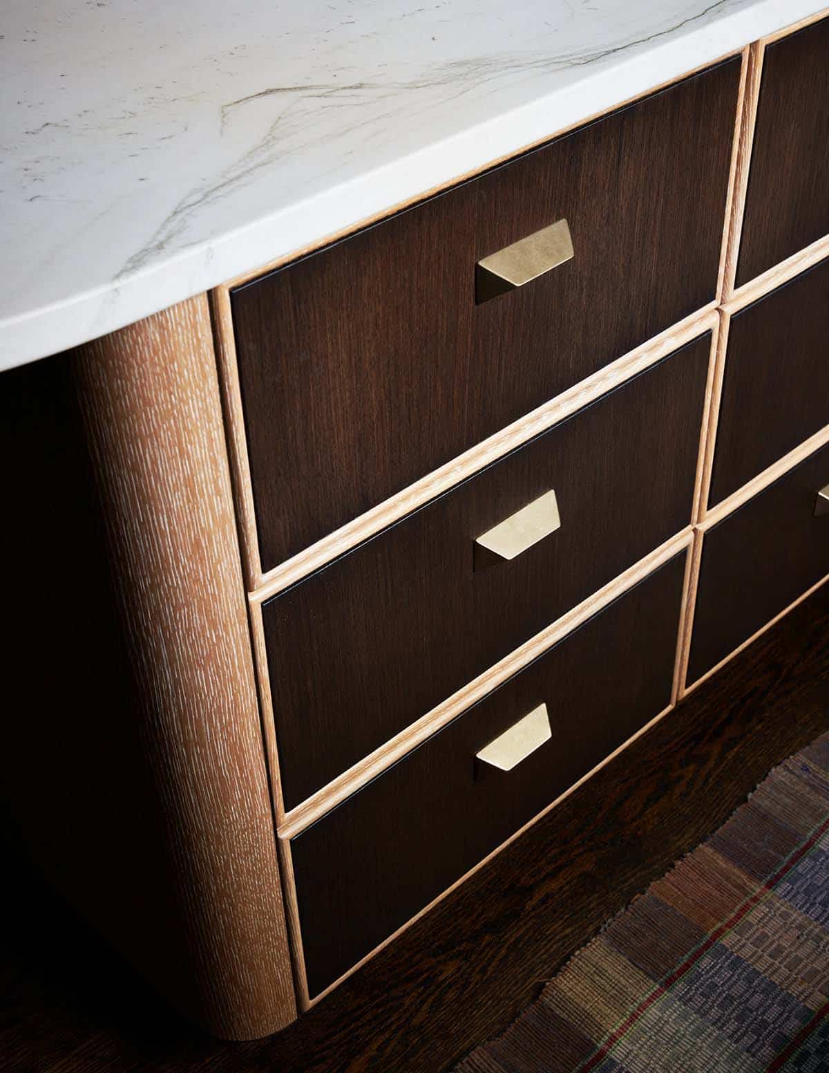 Dark wood island drawers with brass pulls and rounded oak end