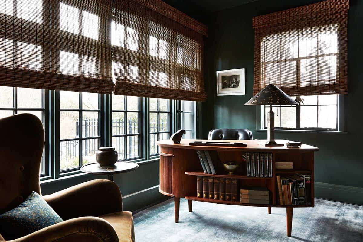 Home office with green walls, woven shades and curved teak desk