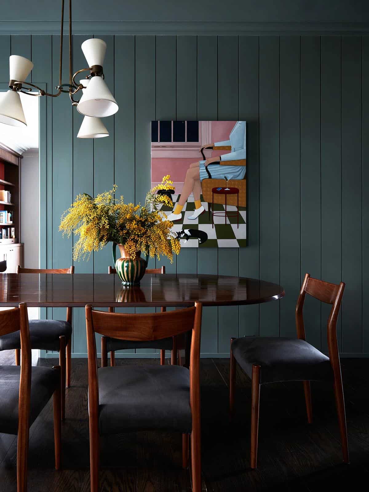 Dining area with green paneled walls, oval table and yellow mimosa