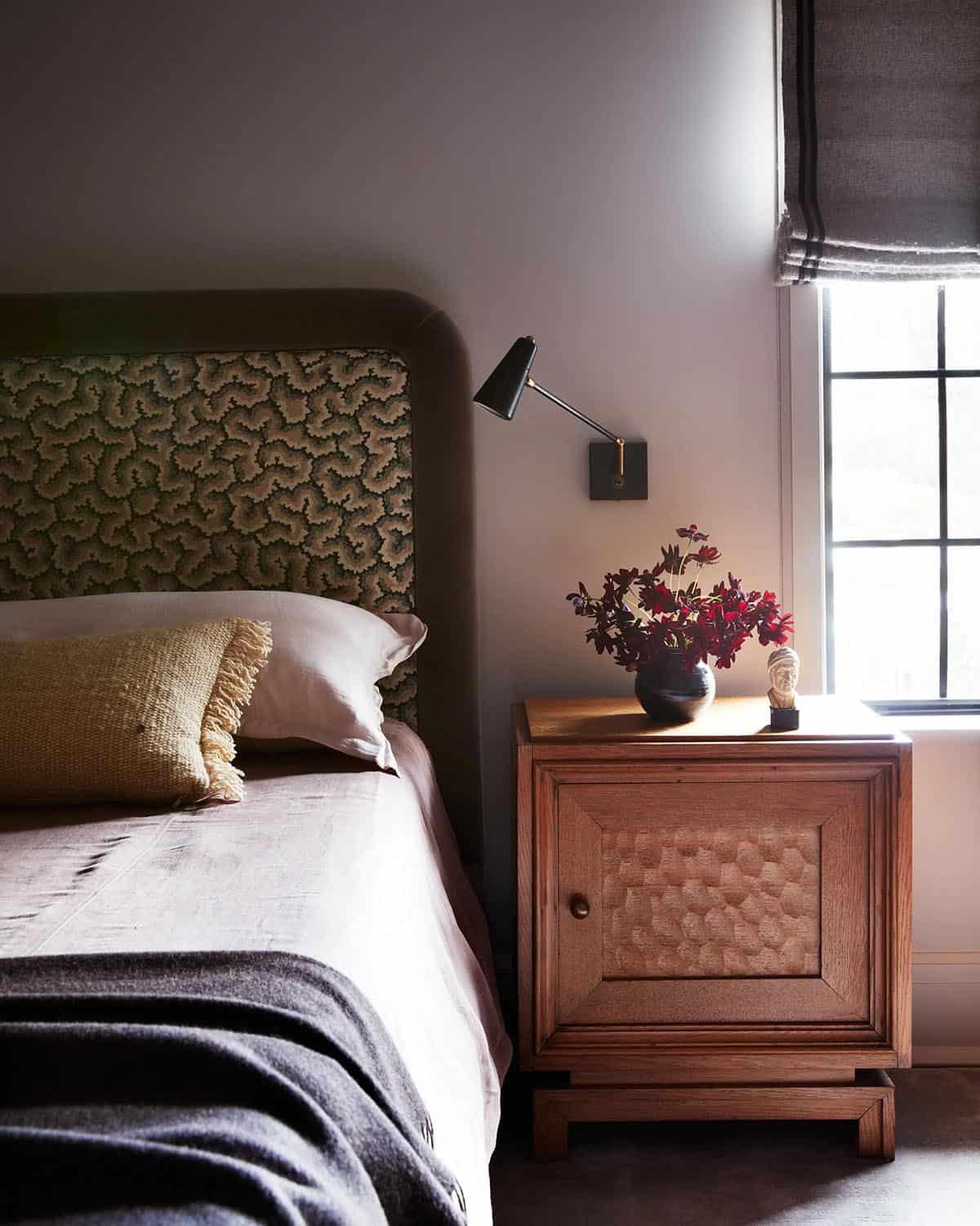 Bed with patterned upholstered headboard beside carved oak nightstand